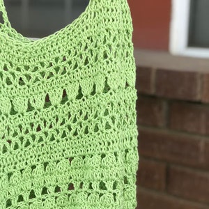 Puede incluir: Una bolsa de mano de crochet de color verde claro con un delicado patr&oacute;n calado.