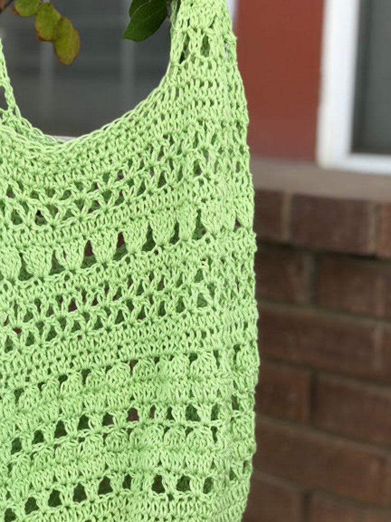Puede incluir: Una bolsa de mano de crochet de color verde claro con un delicado patr&oacute;n calado.
