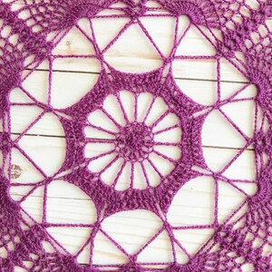May include: A purple crocheted doily with a circular design featuring a central flower motif and repeating geometric patterns.