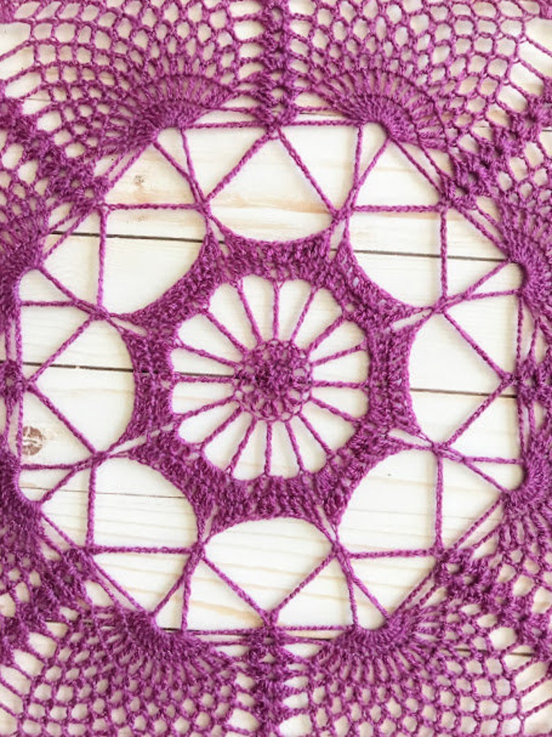 May include: A purple crocheted doily with a circular design featuring a central flower motif and repeating geometric patterns.