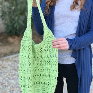 Puede incluir: Una bolsa de mano de crochet de color verde claro con una parte superior ancha y abierta y una sola correa. La bolsa est&aacute; hecha con un delicado patr&oacute;n de punto abierto.