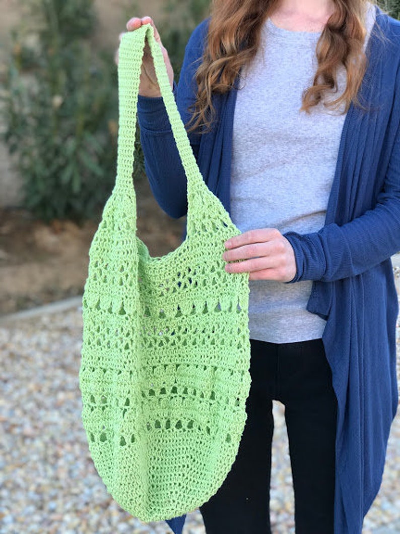 Puede incluir: Una bolsa de mano de crochet de color verde claro con una parte superior ancha y abierta y una sola correa. La bolsa est&aacute; hecha con un delicado patr&oacute;n de punto abierto.