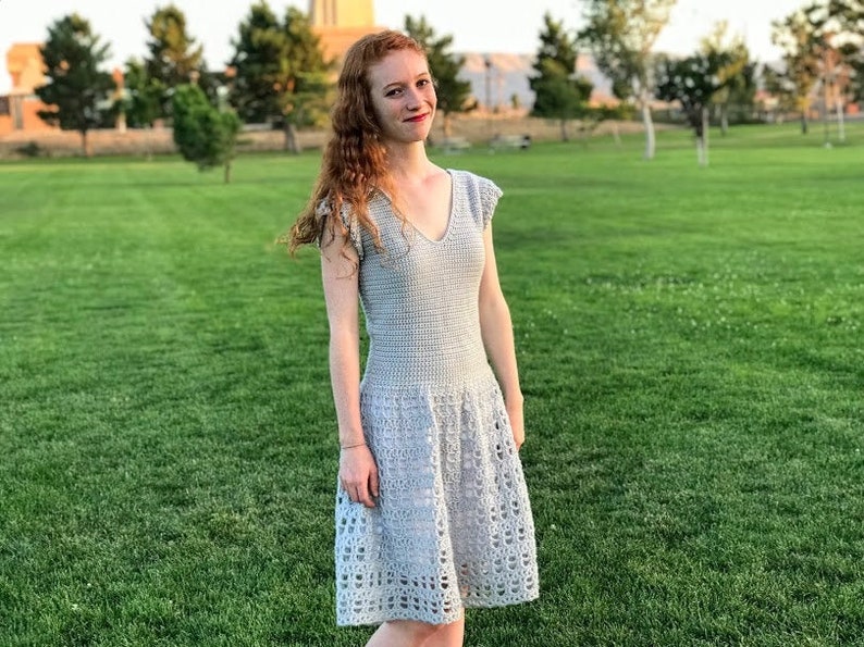 Puede incluir: Una mujer con un vestido de crochet gris claro con cuello en V y falda acampanada.