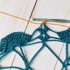 May include: A teal crochet doily with a single orange yarn strand attached to the hook. The hook is labeled "Size H/8 (5.0 mm)".
