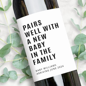 May include: A white wine bottle label with black text that reads "Pairs well with a new baby in the family." Below the text is "Baby Williams Arriving June 2024".
