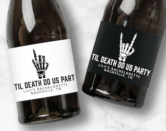 Pode incluir: Duas garrafas de champanhe com rótulos em preto e branco que dizem "Til Death Do Us Part" e "Til Death Do Us Party". Os rótulos apresentam uma mão de esqueleto fazendo um gesto de rock and roll.