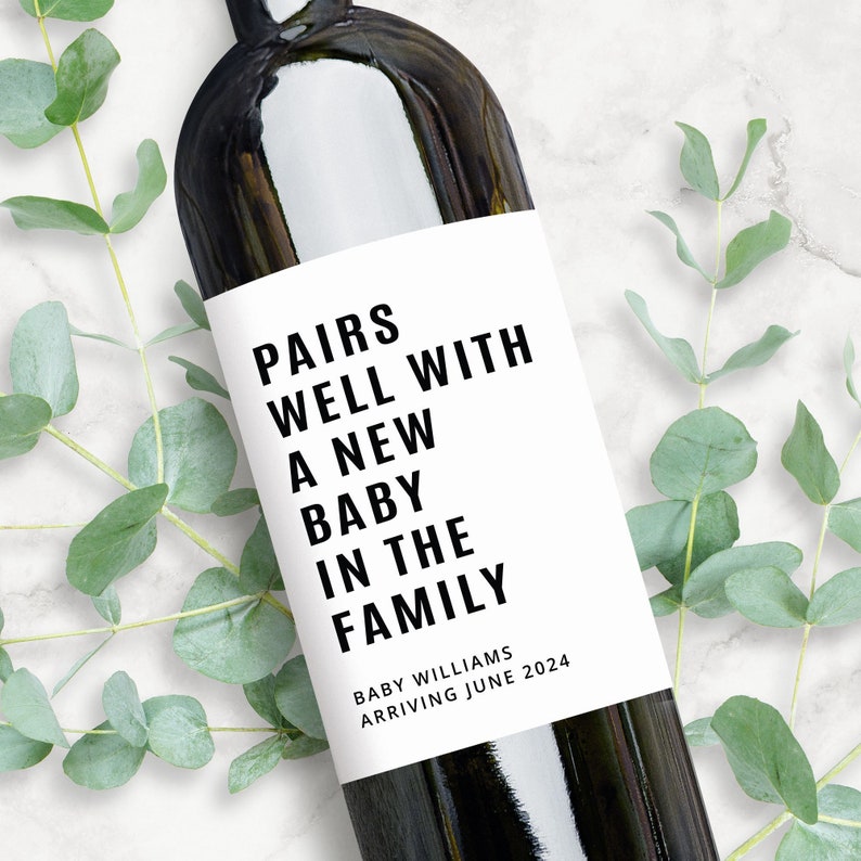 May include: A white wine bottle label with black text that reads "Pairs well with a new baby in the family." Below the text is "Baby Williams Arriving June 2024".
