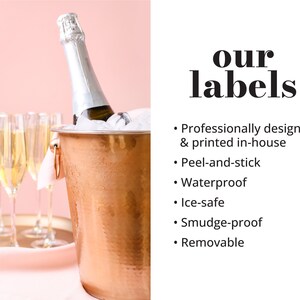 May include: A copper champagne bucket with a bottle of champagne and ice inside. The bucket is on a pink surface with champagne flutes in the background. The text "our labels" is in bold black font with a list of features: professionally designed & printed in-house, peel-and-stick, waterproof, ice-safe, smudge-proof, and removable.