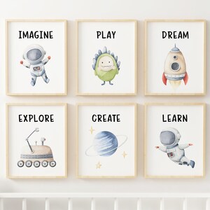 May include: Six framed prints with watercolor illustrations and text. The prints feature an astronaut, a monster, a rocket, a rover, a planet, and another astronaut. The text on the prints reads "Imagine", "Play", "Dream", "Explore", "Create", and "Learn".