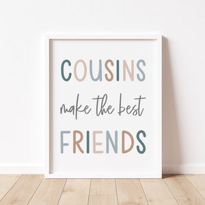以下が含まれることがあります： 白い額縁に入ったプリント。青い、ピンク、茶色の文字で「COUSINS make the best FRIENDS」と書かれている。