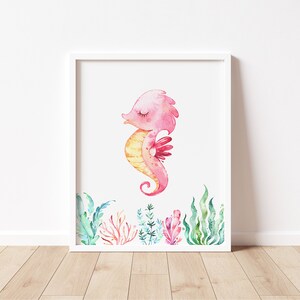 May include: A watercolor illustration of a pink and yellow seahorse with closed eyes, surrounded by green and pink seaweed. The seahorse is in a white frame.