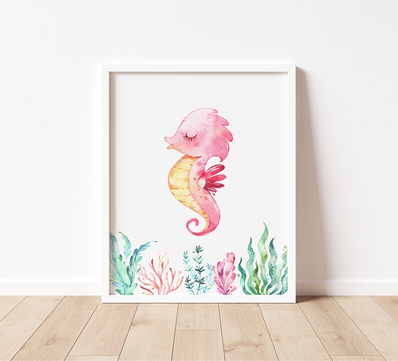 May include: A watercolor illustration of a pink and yellow seahorse with closed eyes, surrounded by green and pink seaweed. The seahorse is in a white frame.