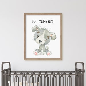 May include: A framed print with a watercolor illustration of a gray and white puppy sitting with the text "BE CURIOUS" above it. The print is hanging on a white wall above a gray crib.