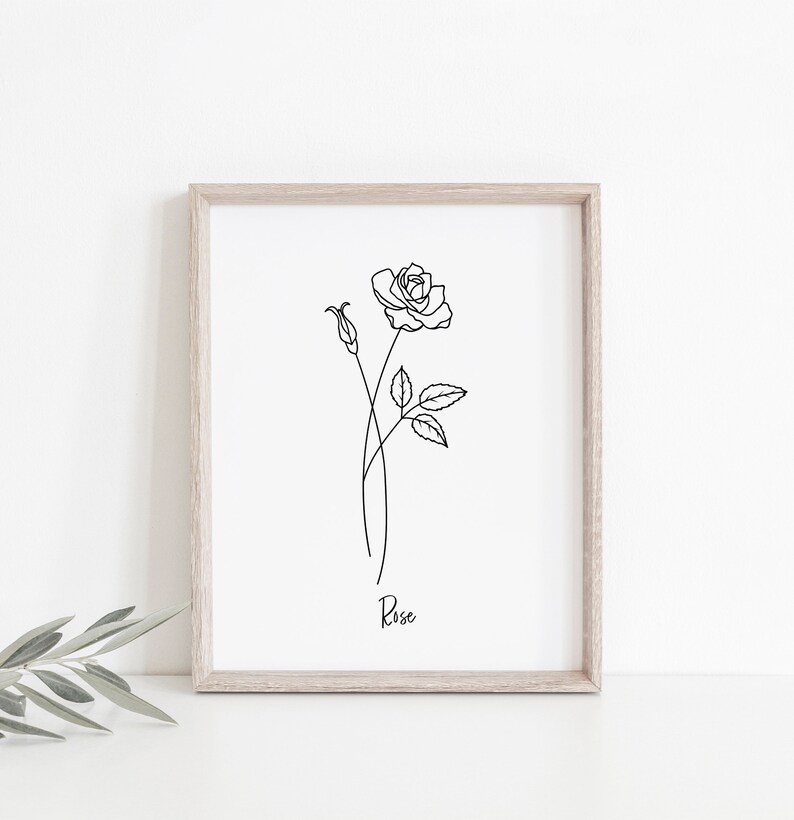 May include: A black and white line drawing of a rose with leaves and a bud. The drawing is framed in a light wood frame and the word "Rose" is written below the drawing.