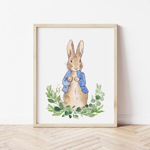 May include: A watercolor illustration of Peter Rabbit wearing a blue jacket, standing in a wreath of green leaves.