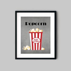 Puede incluir: Una impresi&oacute;n enmarcada con un fondo gris y la palabra "Popcorn" en texto negro. Un cubo de palomitas de ma&iacute;z a rayas rojas y blancas con palomitas de ma&iacute;z amarillas est&aacute; en el centro de la impresi&oacute;n.