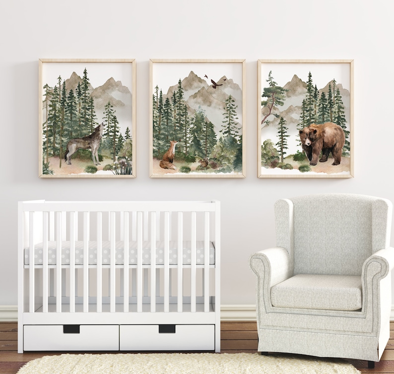 May include: Three watercolor prints of a wolf, a fox, and a bear in a forest setting. The prints are framed in natural wood and hung on a white wall above a white crib with two drawers.