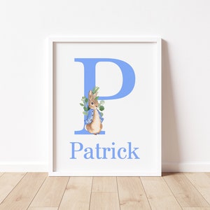 May include: A white framed print with a light blue letter P and a watercolor illustration of a rabbit wearing a blue jacket. The name Patrick is written below the letter.