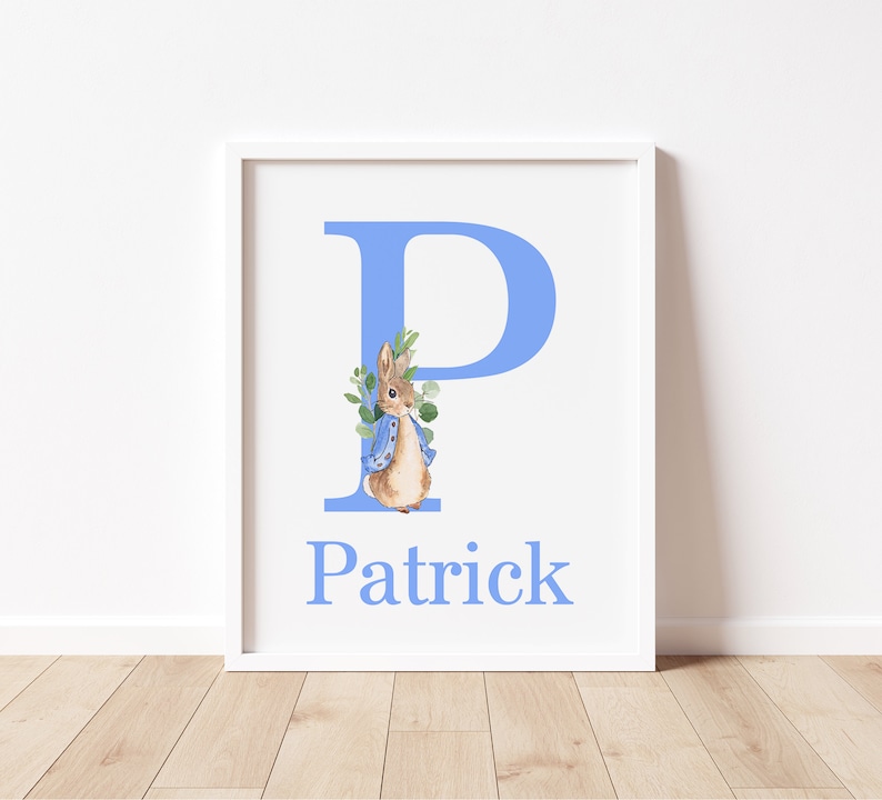 May include: A white framed print with a light blue letter P and a watercolor illustration of a rabbit wearing a blue jacket. The name Patrick is written below the letter.