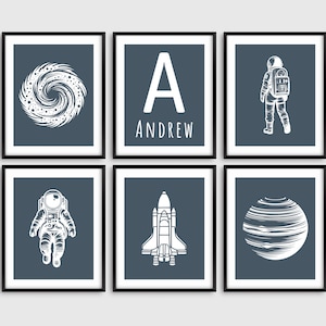 May include: Set of six blue framed prints with white space illustrations of an astronaut, a rocket, a planet, a galaxy, and the letter A with the name Andrew below it.