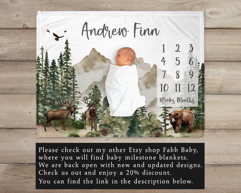 K&ouml;nnte beinhalten: Eine wei&szlig;e Babydecke mit einer Aquarell-Waldszene, Bergen und einem kleinen B&auml;ren. Die Decke ist mit dem Namen "Andrew Finn" personalisiert und enth&auml;lt eine Zahlentabelle, um das Wachstum des Babys in Wochen und Monaten zu verfolgen.