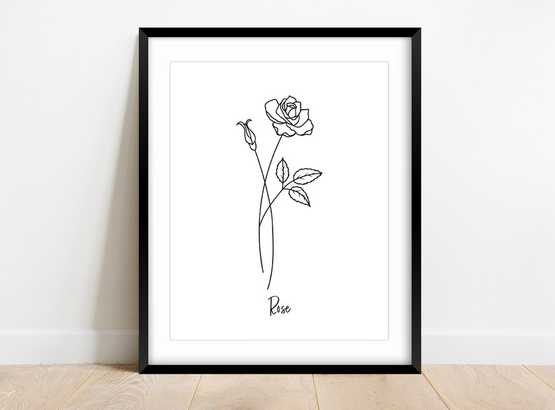 May include: A black and white line drawing of a rose with a bud and leaves. The drawing is framed in a black frame and the word "Rose" is written below the drawing.