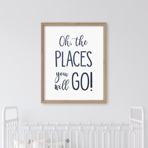 May include: A white framed print with the text "Oh, the PLACES you will GO!" in navy blue script. The print is hanging on a white wall above a white crib.