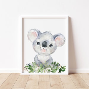 Puede incluir: Una ilustraci&oacute;n de acuarela de un lindo koala con ojos grandes y una dulce sonrisa. El koala est&aacute; rodeado de hojas verdes y flores.