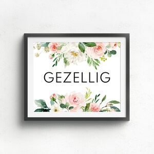 May include: A framed print with a white background and the word "GEZELLIG" in black text. The print is decorated with a watercolor floral border of pink and white flowers and green leaves.