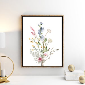 May include: A framed watercolor print featuring a bouquet of wildflowers. The artwork showcases pink, blue, yellow, and white flowers with green foliage against a white background. The frame is a warm gold color.