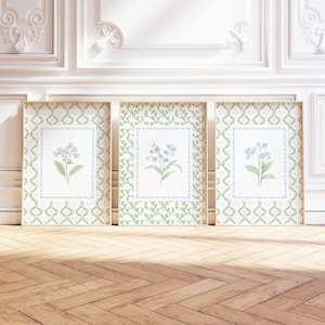 May include: Three framed botanical prints featuring blue forget-me-nots. Each print has a light blue border and is set against a white background. The frames are surrounded by a green and white patterned design. The frames are displayed on a wooden floor.