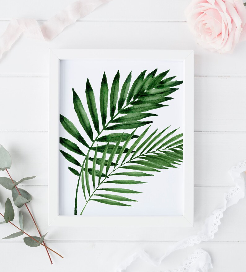 K&ouml;nnte beinhalten: Ein wei&szlig;er Rahmen mit einem Aquarellbild von gr&uuml;nen Palmbl&auml;ttern auf wei&szlig;em Hintergrund.