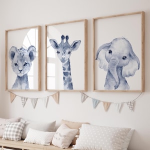 以下が含まれることがあります： 青い色合いの水彩画で描かれた動物の額装されたプリント3枚。プリントにはライオン、キリン、ゾウが描かれています。フレームは天然木製です。