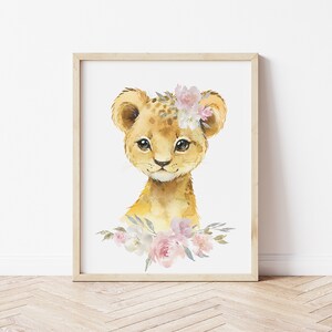 May include: A watercolour painting of a cute lion cub wearing a pink and white flower crown. The lion cub is looking directly at the viewer with big, brown eyes. The background is white.
