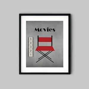 Puede incluir: Una impresi&oacute;n enmarcada en negro con un fondo gris y la palabra "Movies" en texto negro. Una silla de director roja est&aacute; en el centro de la impresi&oacute;n, y una tira de pel&iacute;cula con los n&uacute;meros del 1 al 5 est&aacute; en el lado izquierdo de la impresi&oacute;n.