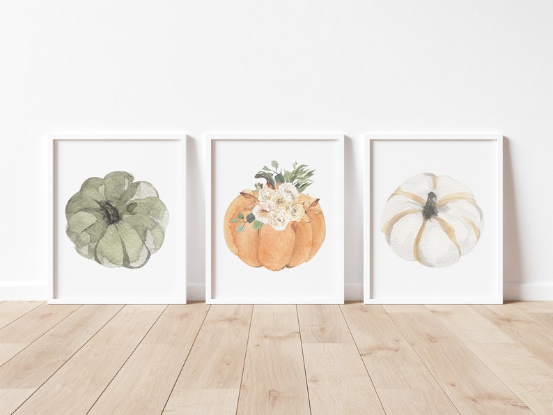 May include: Three watercolor paintings of pumpkins. The first pumpkin is green, the second pumpkin is orange with white flowers, and the third pumpkin is white with gold accents.