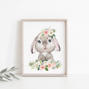May include: A watercolor illustration of a gray bunny wearing a pink and white flower crown. The bunny is surrounded by pink and white flowers and green leaves.