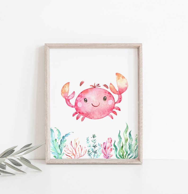 May include: A watercolour painting of a pink crab with a smiling face, surrounded by green and orange seaweed. The crab is in the centre of the image, and the seaweed is around the edges.