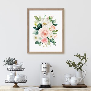 May include: A framed watercolor print of a pink and white floral bouquet with green leaves. The print is hanging on a white wall above a kitchen counter with a coffee maker, mugs, and a tiered serving tray.