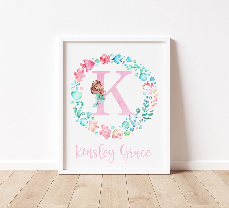 May include: A white framed print with a pink letter K surrounded by a wreath of watercolor sea-themed elements, including a mermaid, seashells, starfish, and anchors. The name Kinsley Grace is written below the letter in pink.