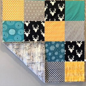 May include: A patchwork baby blanket with a variety of geometric and animal print patterns in teal, gray, black, and yellow. The blanket has a soft, fuzzy gray backing.