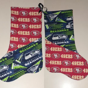 May include: Two Christmas stockings, one red with the San Francisco 49ers logo and the other blue and green with the Seattle Seahawks logo.