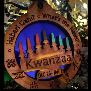 Może przedstawiać: Drewniana ozdoba z niebieskim tłem i tekstem "Habari Gani? What's the News?" oraz "Kwanzaa" z datami "DEC 26-JAN 1".