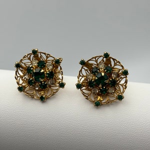 May include: A pair of gold tone clip-on earrings with a filigree design and green and clear rhinestones.