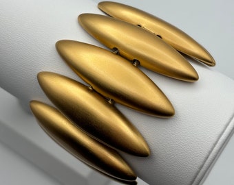 Puede incluir: Un brazalete de oro hecho de múltiples eslabones ovalados. El brazalete está en un expositor blanco.