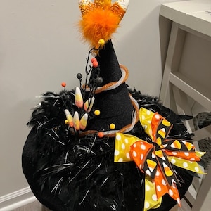 May include: A black witch hat with a large orange and white candy corn bow, black feathers, and a candy corn and orange feather topper.
