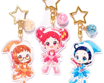 May include: Three colorful character charm keychains with glitter filled charms. Each keychain features a different character with a wand and a star-shaped key ring.