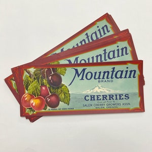 Puede incluir: Etiquetas de cajas de fruta vintage de la marca "Mountain". Las etiquetas muestran ilustraciones de cerezas maduras con hojas verdes. El texto incluye "CHERRIES" y "15 POUNDS NET WHEN PACKED". De Salem Cherry Growers Assn., Salem, Oregon.