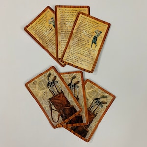 May include: Five cards with a wood grain background and a brown leather golf bag with golf clubs. The cards have text that reads "Articles & Laws in Playing at Goll, 1744".