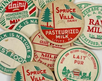 May include: A collection of round, vintage cardboard milk bottle caps featuring various dairy brand names, including Winona Dairy, Spruce Villa Dairy, and others. The caps are printed with red and green text and graphics, such as pine trees and farmhouses.
